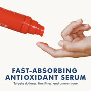 Red cylindrical serum bottle dispensing clear liquid onto a finger above a hand with pale skin.