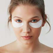 Model using Hydro Cool Firming Eye Gels - Gently applying cooling gel patches under the eyes to hydrate, firm, and reduce puffiness and fine lines with Icelandic glacial water, peptides, and antioxidants for a refreshed, youthful look - Skyn Iceland