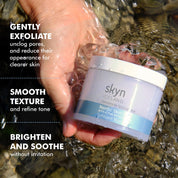 Hand holding Nordic Skin Peel jar with white and light blue label submerged in clear flowing water.