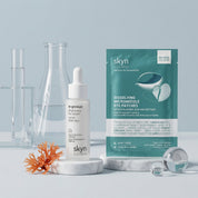 Pair of white and teal skyn eye patches and a white dropper serum bottle with clear laboratory glassware on a pale blue.